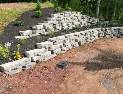 Left angle hardscaped retaining wall at the edge of property with landscaped trees and shrubs