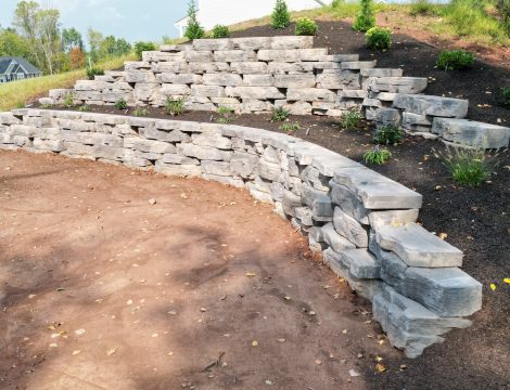 Hardscaped retaining wall at the edge of property with landscaped trees and shrubs