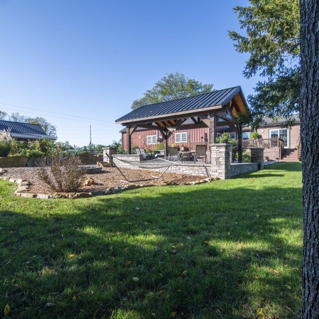 Wide angle photo from back of property showcasing pavilion, hammock, and hardscaped entertainment space