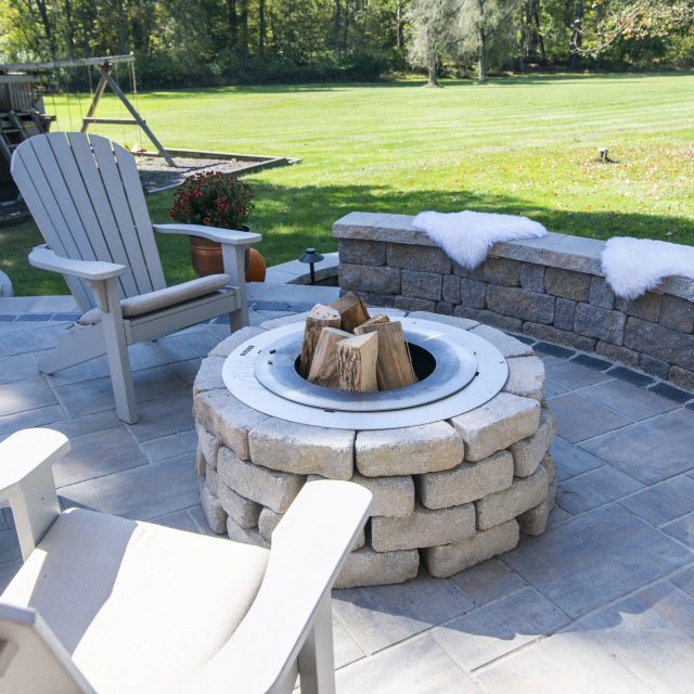 hardscaped fire pit with adirondack chairs and white fuzzy seat mats on retaining wall