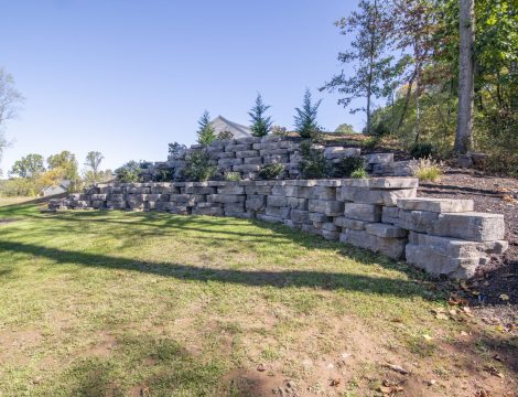 Hardscaped retaining wall at the edge of property with landscaped trees and shrubs