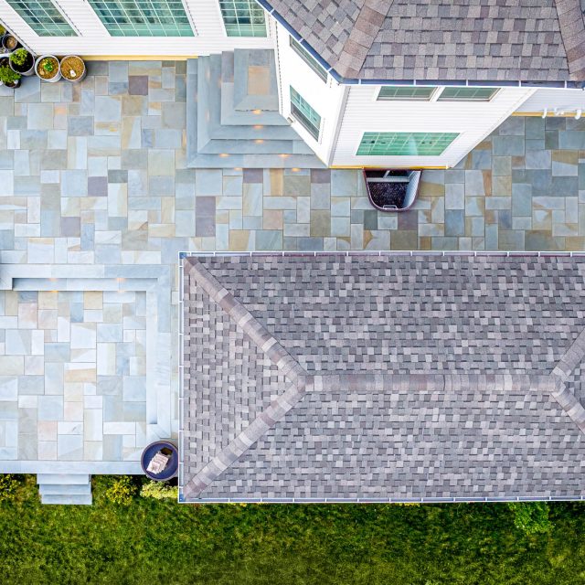 Aerial view of backyard paver patio with pavilion roof, steps, and large stone patio layout behind a house.