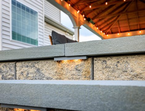 Close-up of stone retaining wall with built-in LED step lighting on a backyard paver patio.