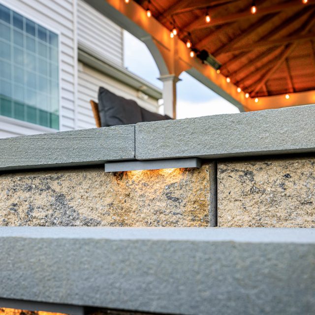 Close-up of stone retaining wall with built-in LED step lighting on a backyard paver patio.