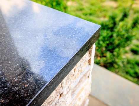 Close-up of polished granite countertop edge on outdoor kitchen island with stacked stone veneer base.