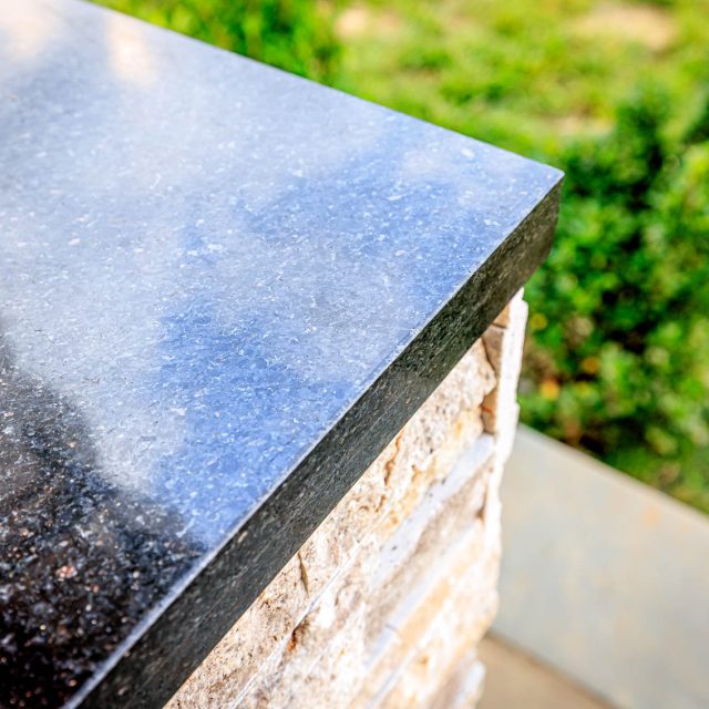 Close-up of polished granite countertop edge on outdoor kitchen island with stacked stone veneer base.