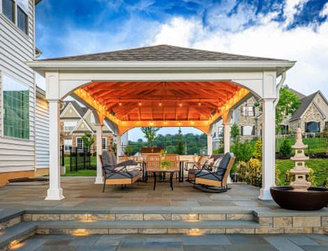 White backyard pavilion with string lights, outdoor dining set, and paver patio with illuminated steps.