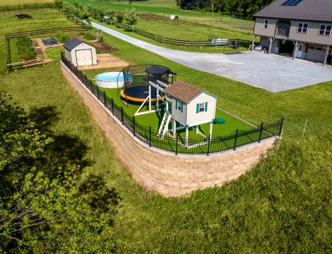 Aerial view of elevated backyard with retaining wall, aluminum fence, pool and playset