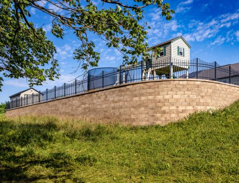 Curved tan retaining wall with black aluminum fence around elevated backyard