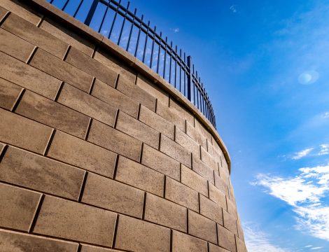 Low angle view of curved block retaining wall with black fence against blue sky