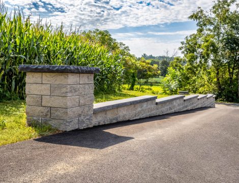 Concrete block retaining wall with square pillar and cap along asphalt driveway
