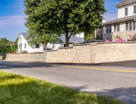 Concrete block retaining wall running along residential roadside with tiered sections