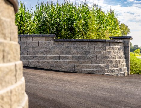 Curved concrete block retaining wall with capstone bordering asphalt driveway
